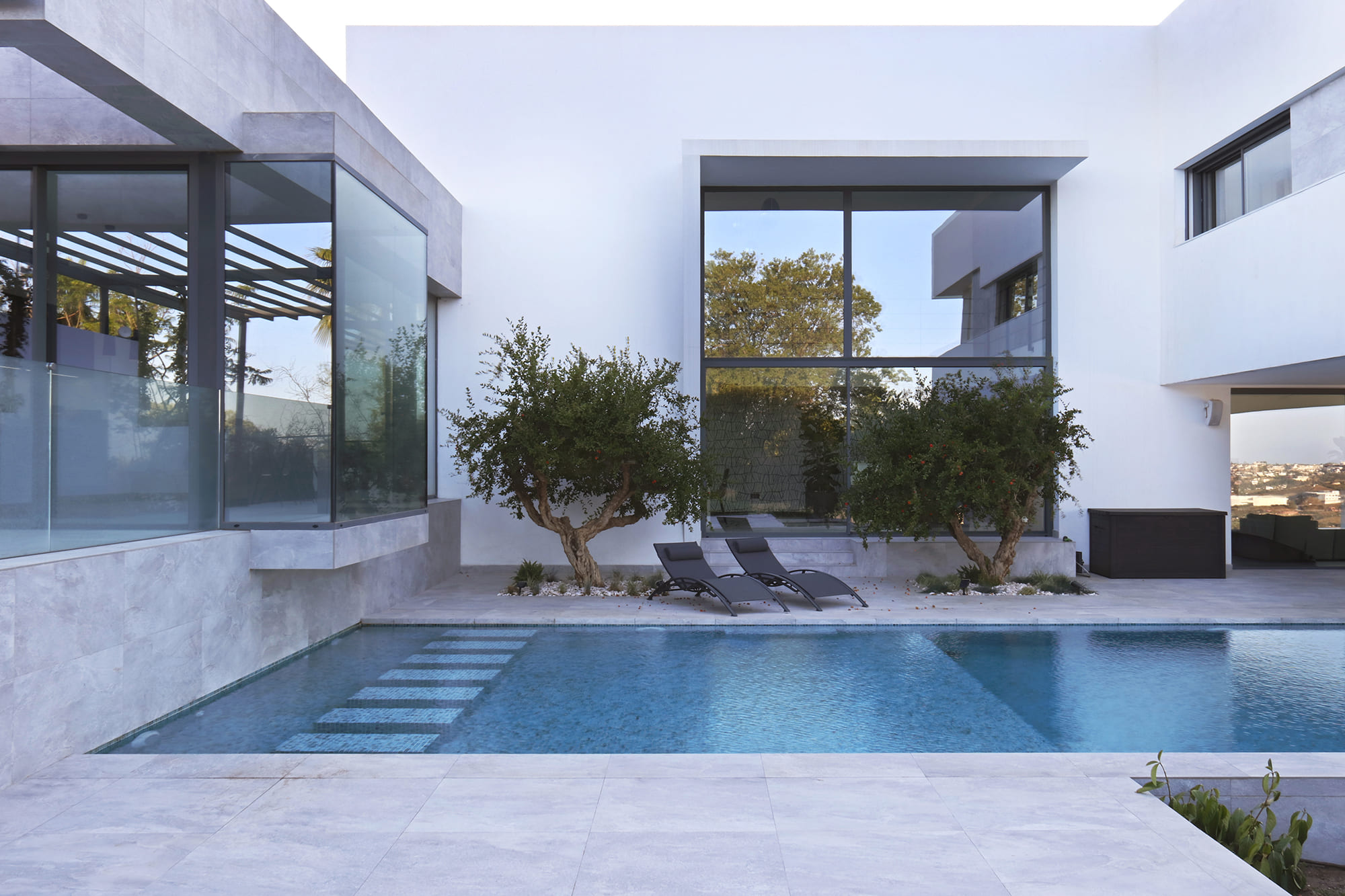 Vista lateral de la villa en voladizo sobre la ladera, con piscina y tumbonas junto al olivar