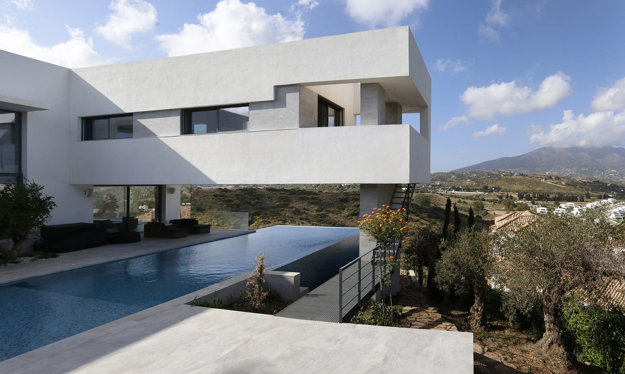 Vista panorámica de la villa en voladizo, piscina infinita y ladera mediterránea al fondo