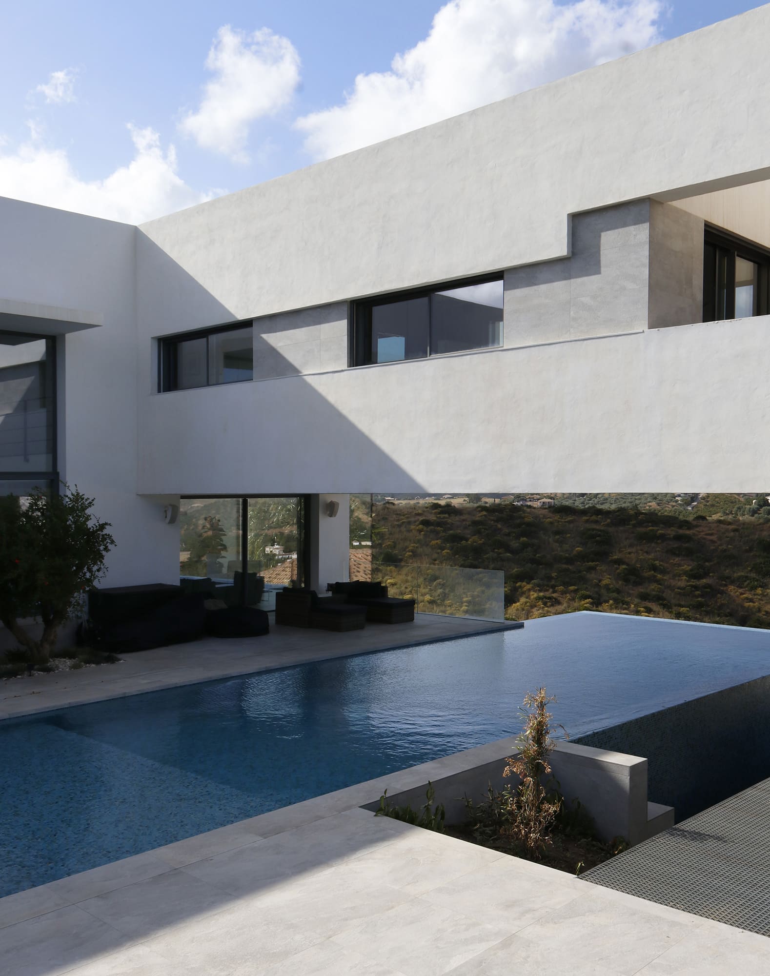 Detalle del voladizo blanco y ventanales con barandilla de vidrio, integrados en el paisaje