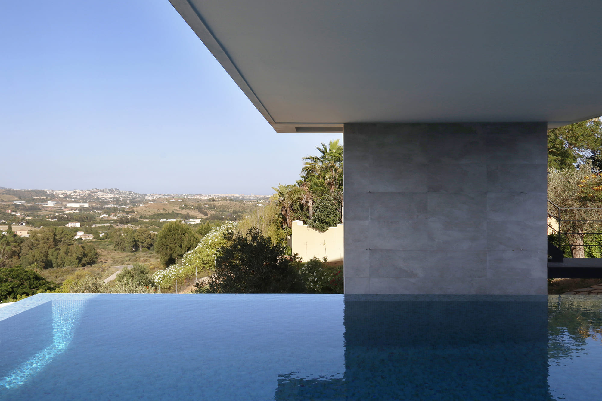 Hombre de pie en la terraza bajo el voladizo, con vistas a la piscina y al horizonte