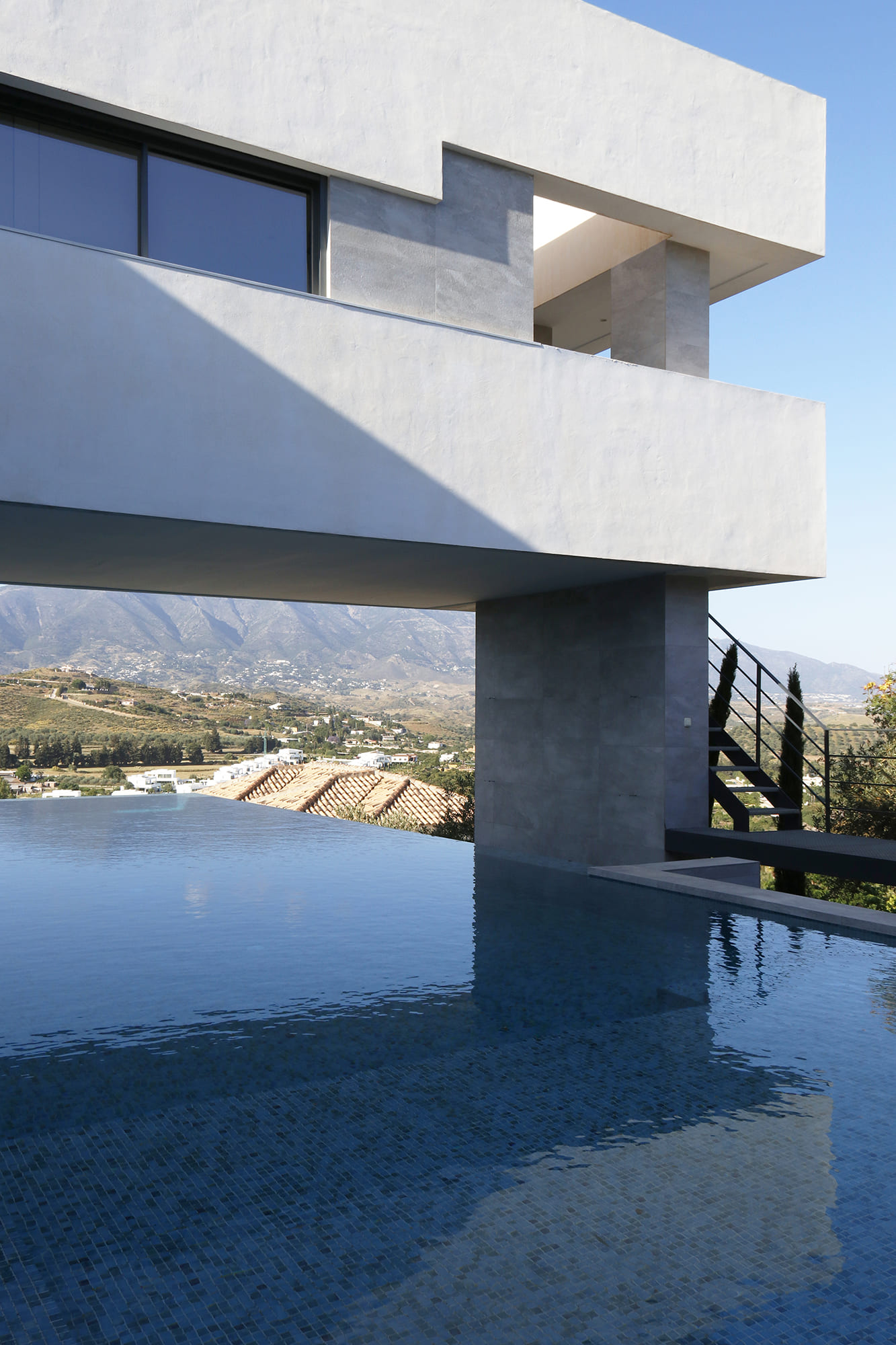 Primer plano de la piscina infinita reflejando el voladizo y la ladera mediterránea