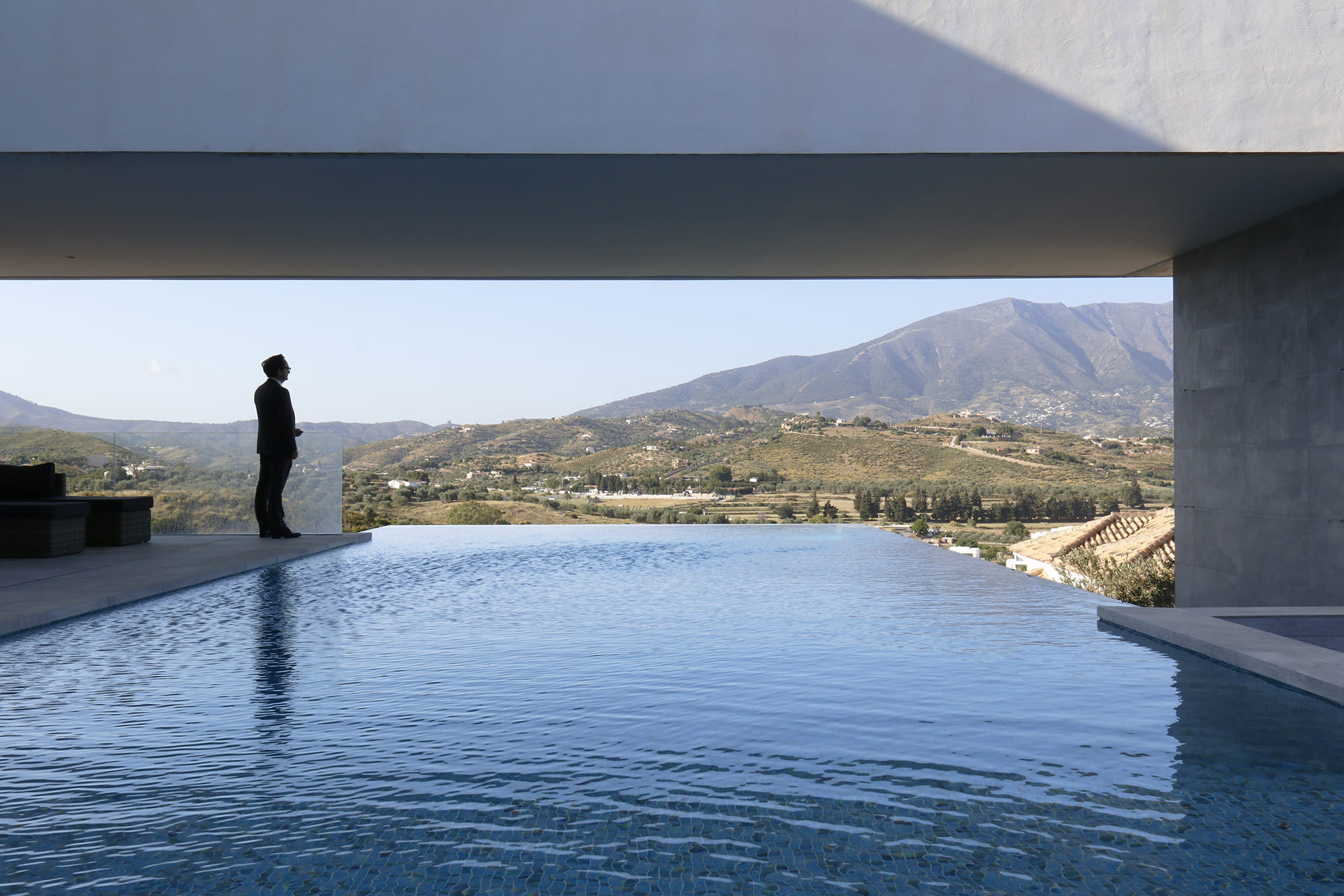 Perfil en silueta mirando desde la piscina al paisaje de montañas y olivos