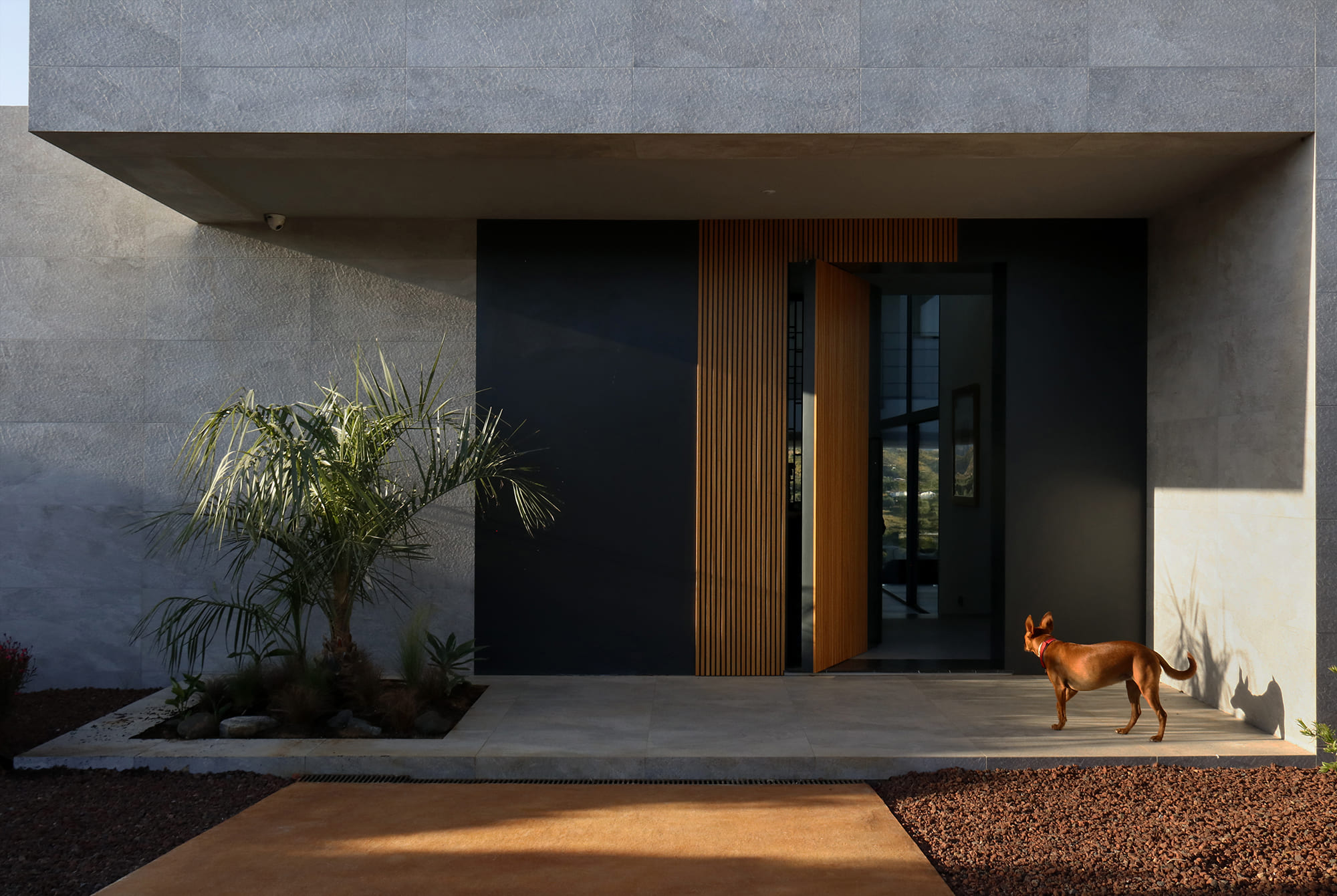 Vista frontal del gran pórtico de hormigón visto y muro de piedra que enmarca la entrada principal