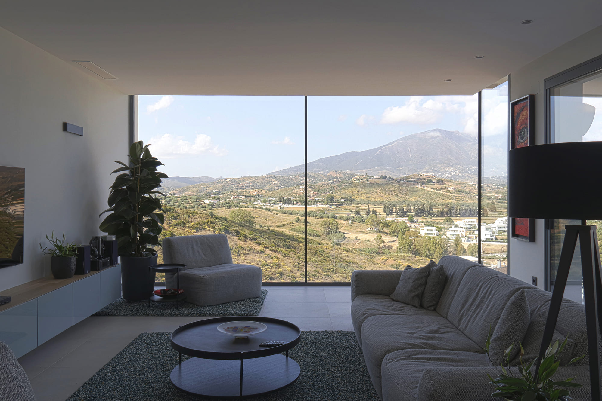 Salón con piano blanco, sofá gris y grandes ventanales que abren al valle mediterráneo