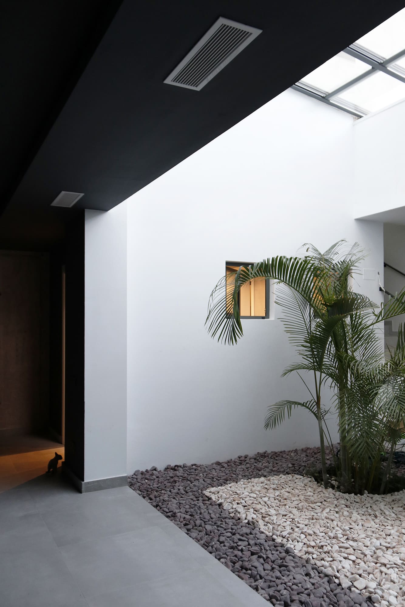 Patio interior con lucernario de vidrio, jardineras y contraste de pavimento claro y oscuro