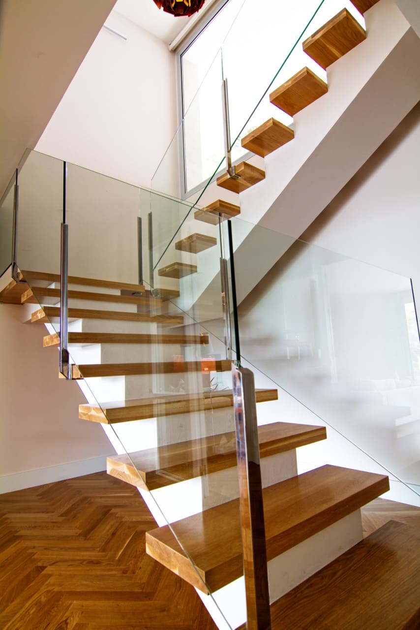 Escalera flotante de madera con barandilla de cristal que conecta la planta baja con la superior en la Vivienda P∩C