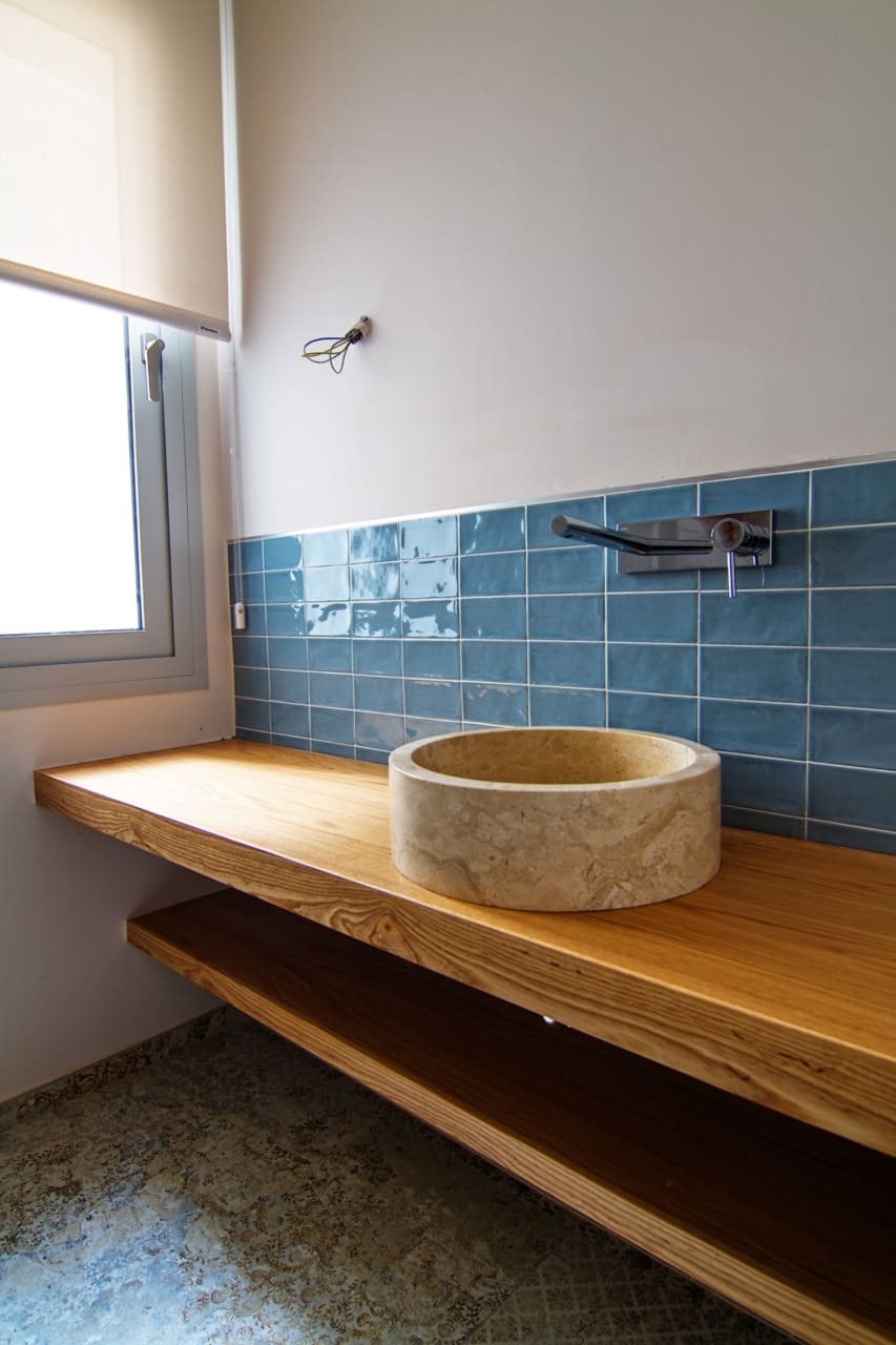 Detalle de baño en la Vivienda P∩C con lavabo de piedra, encimera de madera y alicatado cerámico azul